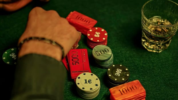 Businessman grabbing poker chips on green table with whiskey