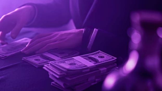 Businessman counting large stacks of hundred dollar bills under purple light