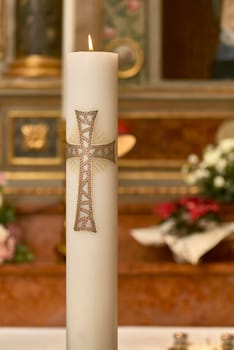 Lit paschal candle with decorative cross symbolizing jesus christ resurrection in a blurred church interior
