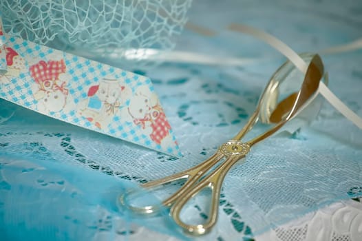 Elegant silver serving tongs are placed on a delicate blue lace fabric, accompanied by a decorative ribbon, creating a refined table setting