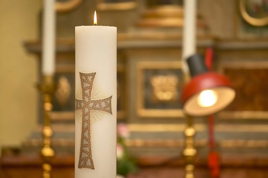 Lit paschal candle with decorative cross burning in a church, symbolizing christian faith and celebration
