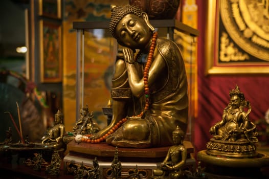 Golden buddha statue meditating serenely with mala beads in a peaceful buddhist temple, surrounded by other religious artifacts