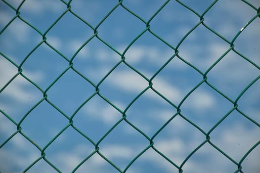 Close up of a green wire mesh fence with a blue sky and clouds in the background