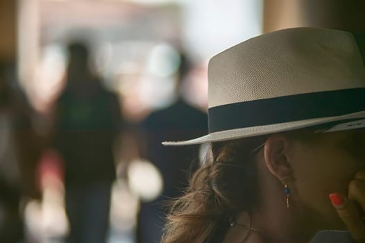 Stylish woman wearing panama hat standing in a blurred crowd, enjoying a casual outing
