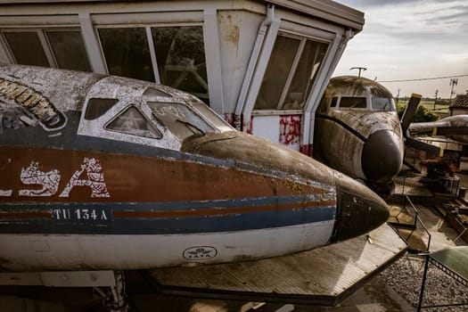 Old rusty abandoned airplane fuselage near a control tower, showing signs of decay and weathering