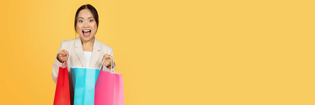 Surprised glad young japanese lady shopaholic open colorful bags, with purchases enjoy shopping, isolated on orange studio background. Huge sale, lifestyle and new fashion