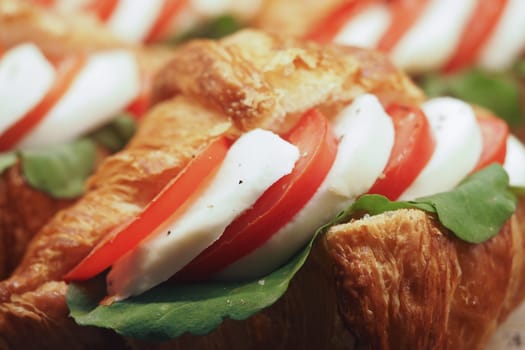 A tasty croissant filled with juicy tomato, rich mozzarella cheese, and fresh greens