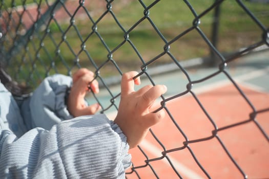 A childs small hands clutching a fence, showing their curiosity and playful spirit