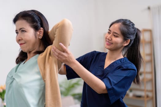 A caregiver helps an elderly woman change clothes in a warm inviting home environment.