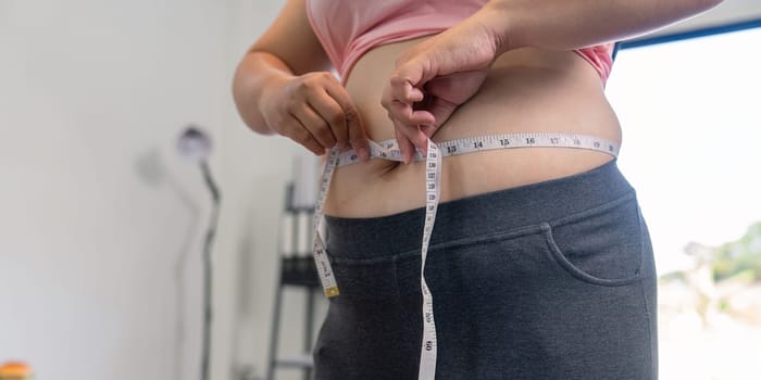 A person measures their waist reflecting a journey of weight loss and health improvement at home.