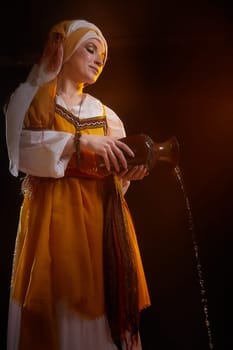A girl in traditional eastern attire gracefully pours water from a clay pot, illuminated by warm, dramatic lighting.