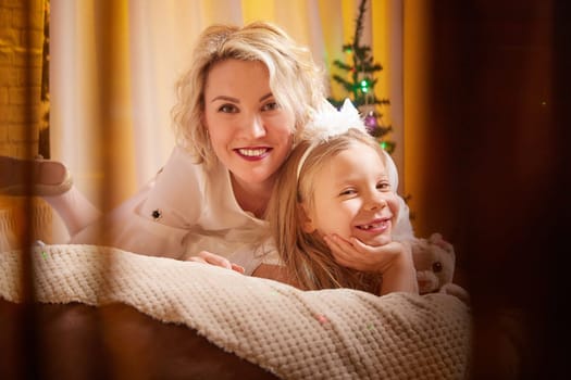 Mother and daughter smile together near a decorated Christmas tree, enjoying the festive atmosphere of the holidays.