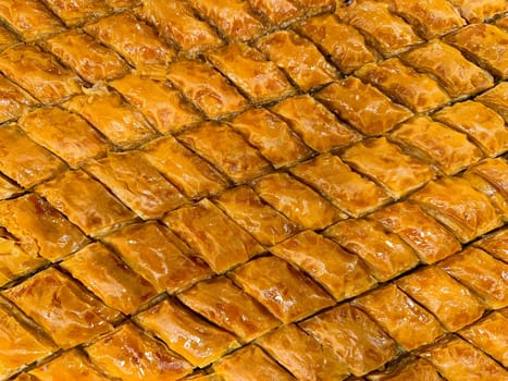 Solid background of freshly baked baklava laid out in rows, golden brown with syrup glaze, traditional Middle Eastern sweet pastry dessert, close up texture. Ramadan concept. High quality photo