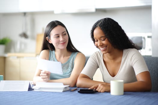 Two interracial roommates calculating expenses in the kitchen at home