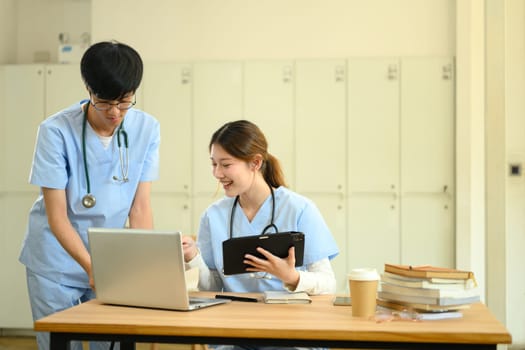 Two medical students discussing and analyzing information on a laptop in modern study area.