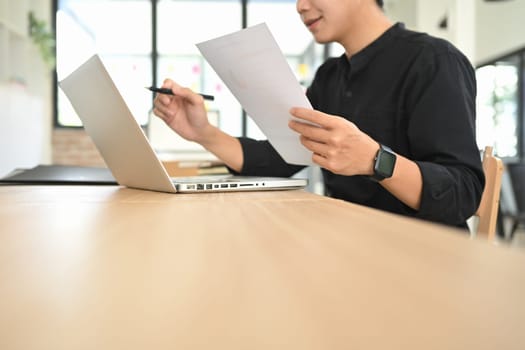 Focused businessman reviewing report while working on a laptop.