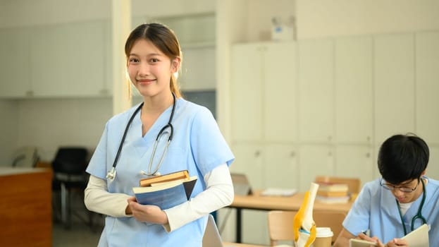 Medical student holding textbooks and smiling confidently at camera.