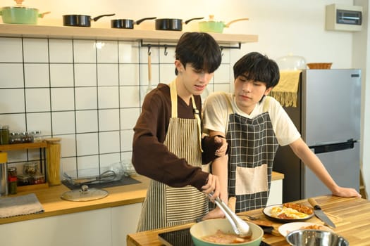Happy gay couple in aprons preparing a delicious meal together in modern kitchen.