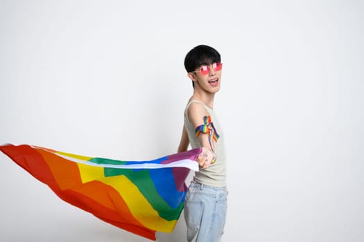 Cheerful gay man posing dynamically with a pride flag against white background.