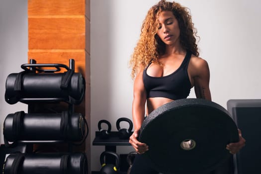 concentrated muscular sportswoman standing with heavy weight plate during workout in gym, concept of fitness and active lifestyle