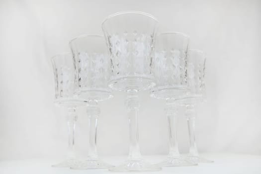 Crystal wine glasses with expanded edges and faceted pattern stand in a wedge on a white background, the first glass in focus, the others are in focus on both sides of him, bottom view. High quality photo
