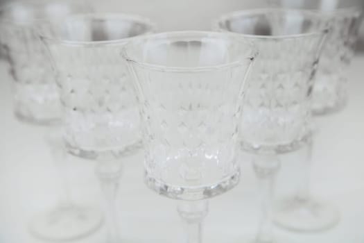 Crystal wine glasses with expanded edges and faceted pattern stand in a wedge on a white background close-up. High quality photo