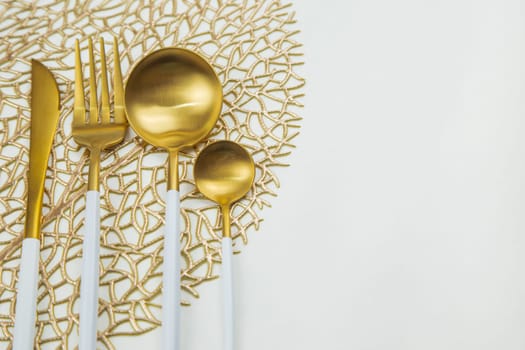 Cutlery knife, fork, spoon and teaspoon with gold color with white handle lie on a napkin of gold color on a white background. The concept of food, culture, and eating. High quality photo