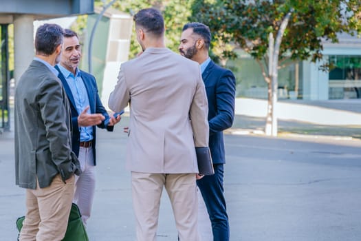 Group of four businessmen in formal and smart casual attire discussing outdoors in a modern urban setting, demonstrating teamwork and collaboration.