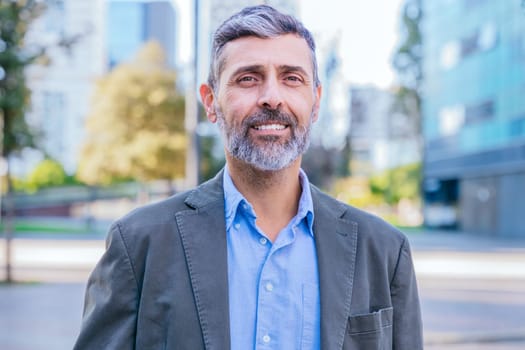 Portrait of a smiling middle-aged businessman in a smart casual outfit standing outdoors in a modern urban environment, exuding confidence and professionalism.