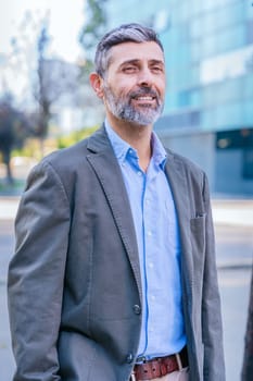 Portrait of a smiling middle-aged businessman in a smart casual outfit standing outdoors in a modern urban environment, exuding confidence and professionalism.