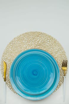 Bright blue serving plates stand on golden air-twisted napkins, on the sides are a golden knife and fork with white on a white background. The concept of serving. The concept of eating. High quality photo