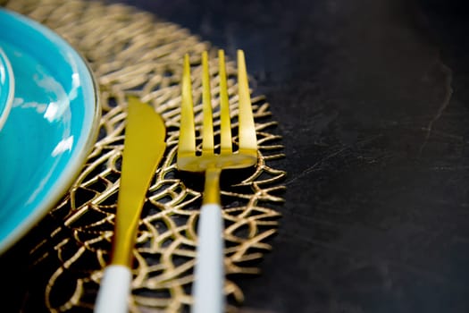 Close-up. View of the part of the blue plates stand one on one on a gold patterned napkin, gold cutlery lies on the side: a fork and a knife on a black background. The concept of serving, the culture of eating. High quality photo