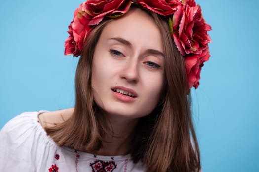 A girl with long hair wears a white embroidered shirt adorned with colorful patterns while a crown of vibrant flowers rests on her head.