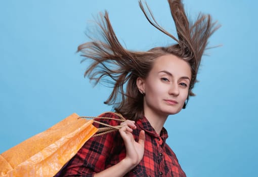 A joyful young woman playfully tosses her hair while holding colorful shopping bags. The bright backdrop enhances her cheerful expression, showcasing the excitement of the shopping season.