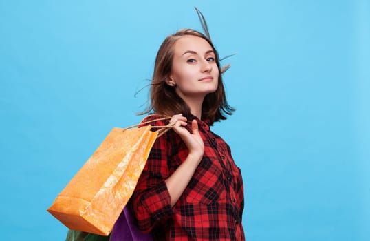 A young woman confidently poses with vibrant shopping bags against a bright blue background. She embodies the excitement of the shopping season, perfect for fashion enthusiasts.