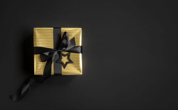 Banner with gold gift box and black ribbon on a black background. Top view, copyspace.