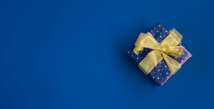 Banner with a blue gift box with golden ribbon on blue background. Top view. Space for text.