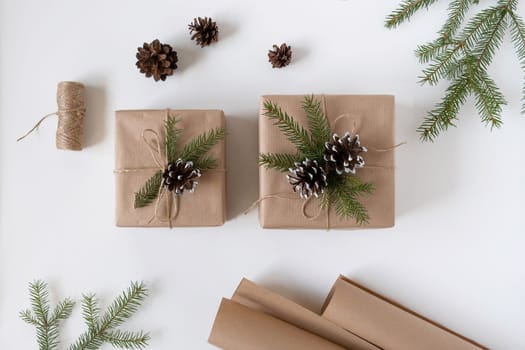 Two gift boxes in craft paper with spruce branches and cones with packing accessories on a white background top view