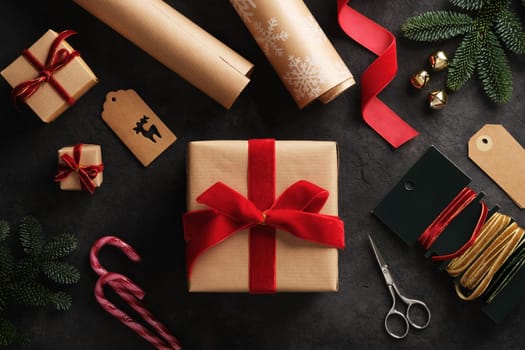 Holiday preparation, wrapped gift in a kraft brown box with red velvet ribbon and gift wrapping supplies all around