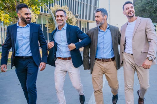 Four businessmen in smart casual and formal attire walking outdoors in an urban setting, smiling and engaging with each other, showcasing teamwork and camaraderie.