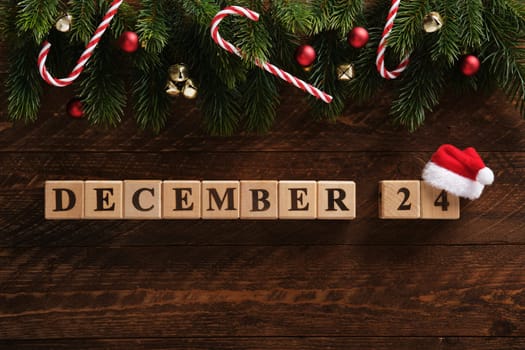 Date December 24 on a dark wooden background with fir sprigs, Christmas tree balls, bells and sugar canes. Festive background.