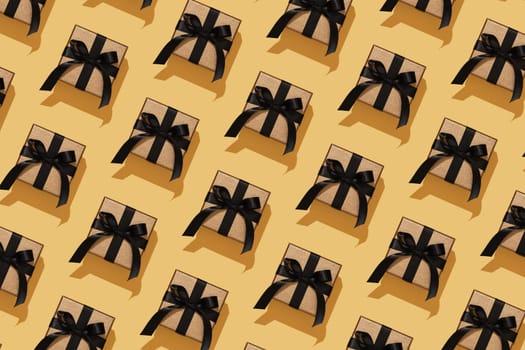 Elegant gold coloured gift boxes with black bows on a yellow background. Festive pattern.