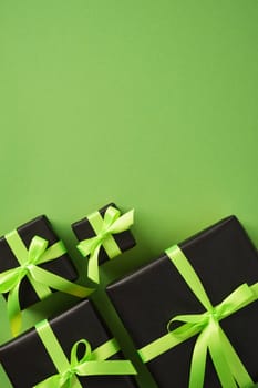 Gift boxes in black wrapping paper with neon green ribbons, set on green background. Space for your text.