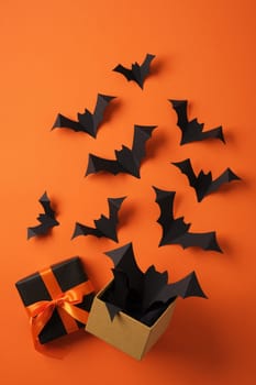 Paper bats flying out of gift box on orange backdrop. Background for Halloween cards, banners, invitations.