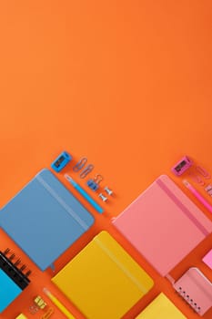 Banner with blue, yellow and pink notepads and colored office supplies on a bright orange background. Copyspace.