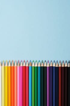 Colored pencils lie flat on a ruler on a light blue background. Space for your text