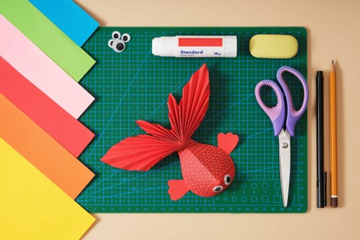 Paper fish craft and paper crafting tools. Scissors, colored paper, glue, paper cutting mat, felt-tip pen. Top view
