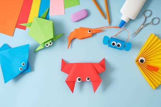 Finished origami red paper toy crab. On the table are other finished toys fish, stingray, turtle, shrimp. DIY project concept for kids. Flat lay