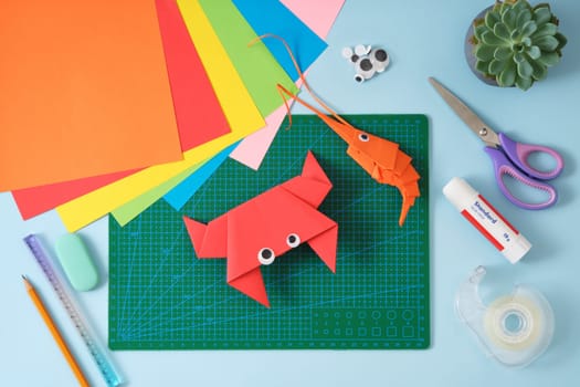 Top view of paper cutting tools, scissors, cutter, and crab and shrimp paper craft toys. DIY project concept for kids. Flat lay