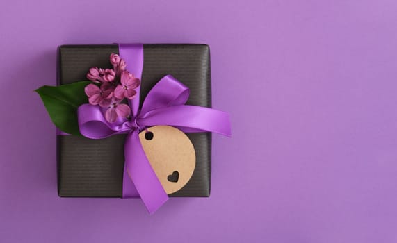 Gift box with lilac flowers and empty gifttag on violet background. Space for your text.